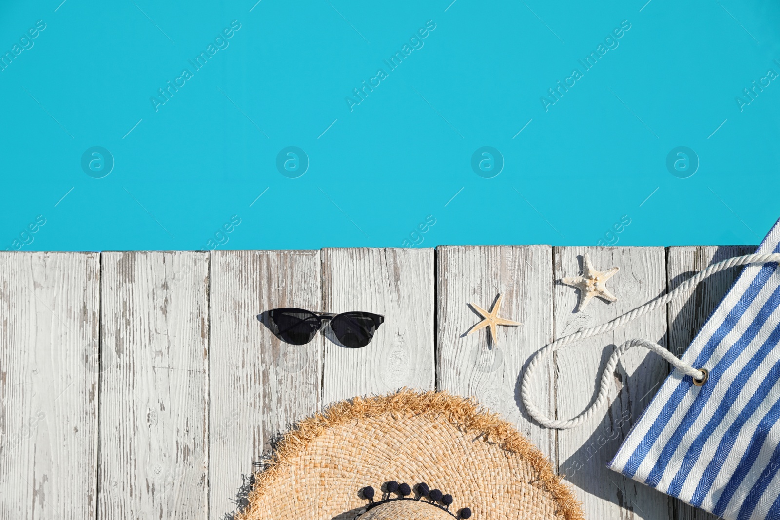 Photo of Beach accessories on wooden deck near outdoor swimming pool, flat lay. Space for text