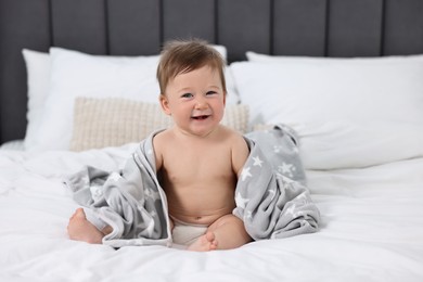 Happy baby boy with blanket sitting on bed at home