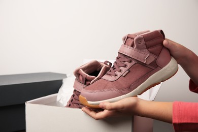 Photo of Girl taking out new sneakers from box against light grey background, closeup