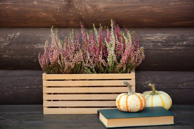 Beautiful heather flowers in crate, book and pumpkins on table near wooden wall