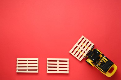 Toy forklift and wooden pallets on red background, flat lay. Space for text