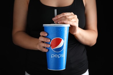 Photo of MYKOLAIV, UKRAINE - JUNE 9, 2021: Woman holding paper Pepsi cup on black background, closeup