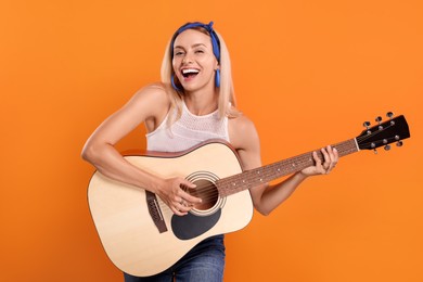 Happy hippie woman playing guitar on orange background