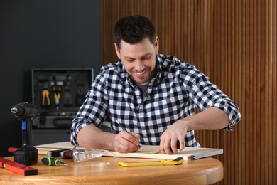 Photo of Handsome working man making marks on timber at table indoors. Home repair