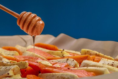 Pouring honey onto slices of parsnip and carrot against blue background, closeup