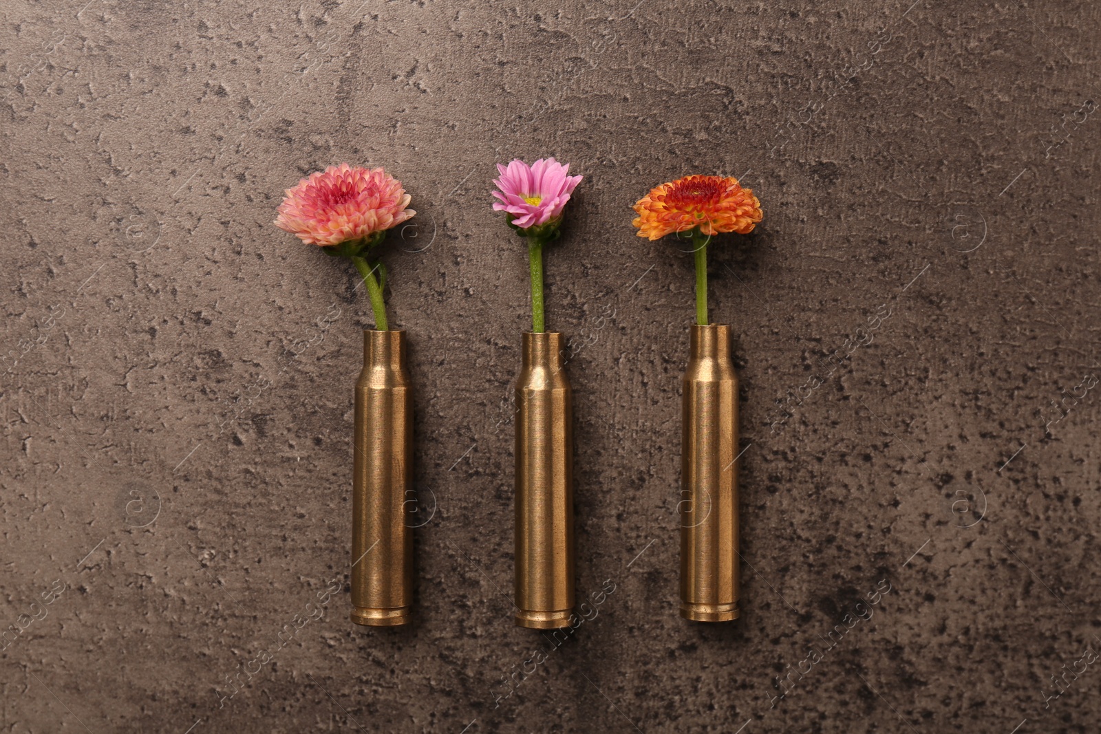 Photo of Beautiful flowers in bullet cases on grey textured table, flat lay