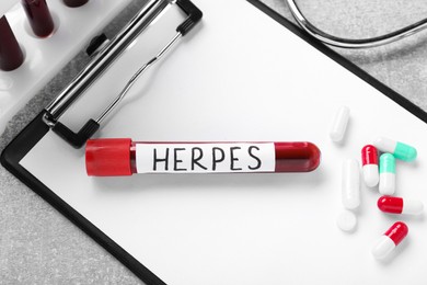 Photo of Test tube with word Herpes, different pills and clipboard on light grey table, flat lay