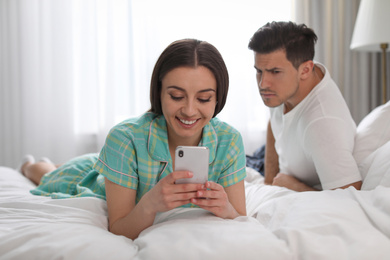 Distrustful man peering into girlfriend's smartphone at home. Jealousy in relationship