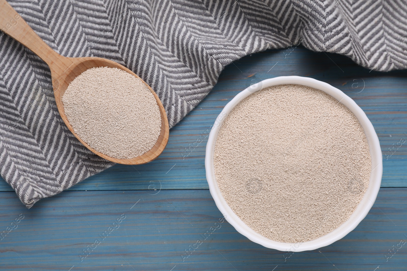 Photo of Bowl and spoon with active dry yeast on light blue wooden table, top view