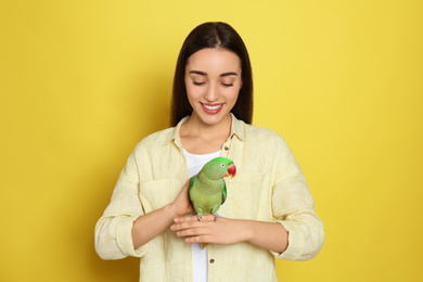 Young woman with Alexandrine parakeet on yellow background. Cute pet