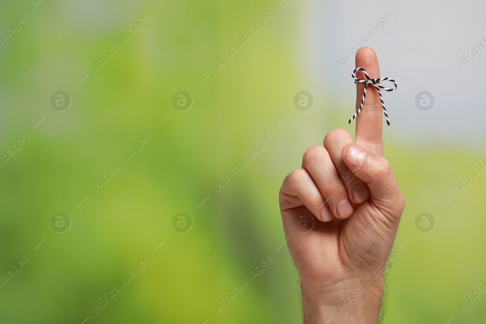 Photo of Man showing index finger with tied bow as reminder on green blurred background, closeup. Space for text