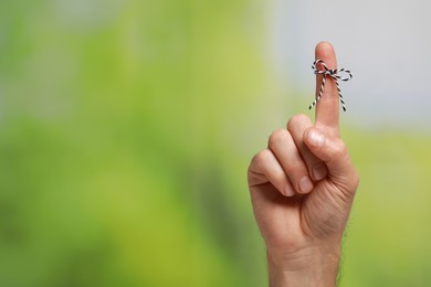 Photo of Man showing index finger with tied bow as reminder on green blurred background, closeup. Space for text