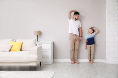 Photo of Father and son comparing their heights near wall in living room