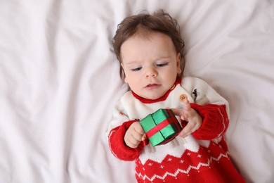 Photo of Cute little baby with gift on soft bed, top view. Space for text