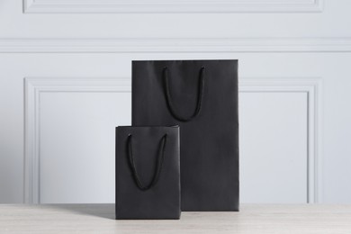 Photo of Black paper bags on wooden table against light grey wall