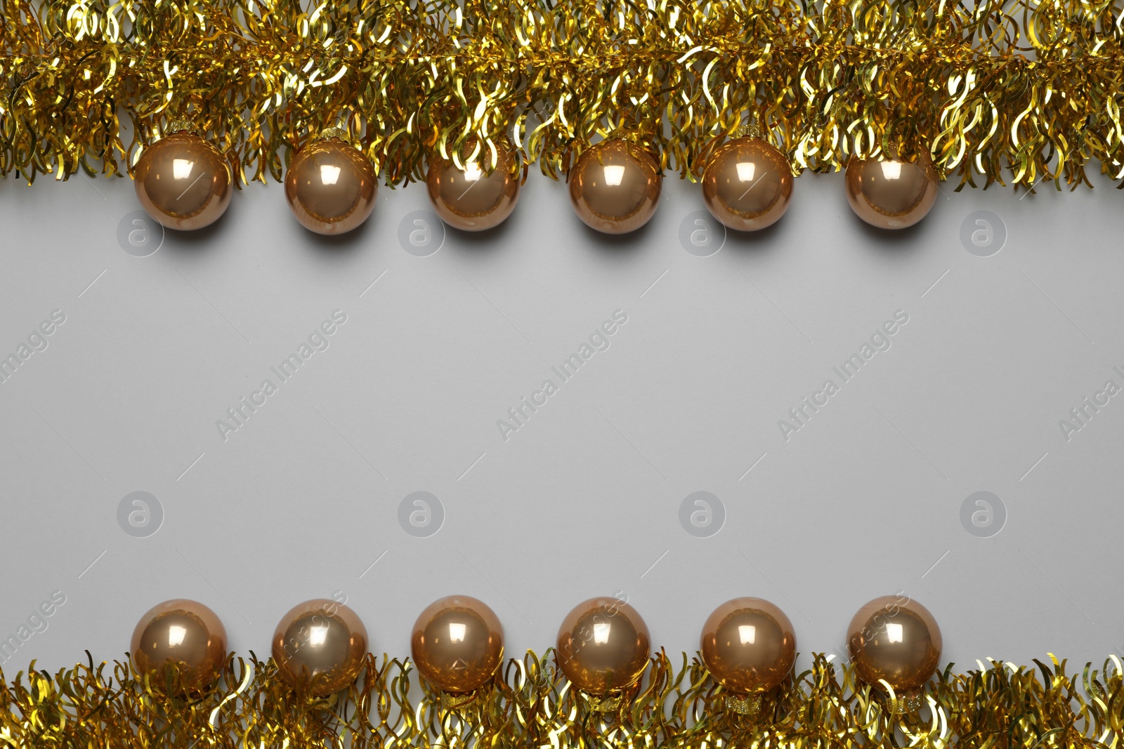 Photo of Golden tinsel and Christmas balls on light grey background, flat lay. Space for text