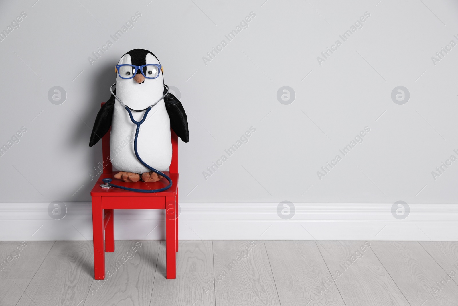 Photo of Toy penguin with eyeglasses and stethoscope near white wall, space for text. Pediatrician practice