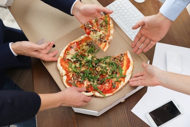 Photo of Office employees having pizza for lunch at workplace, closeup. Food delivery
