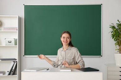 Beautiful young teacher giving lesson at table in classroom