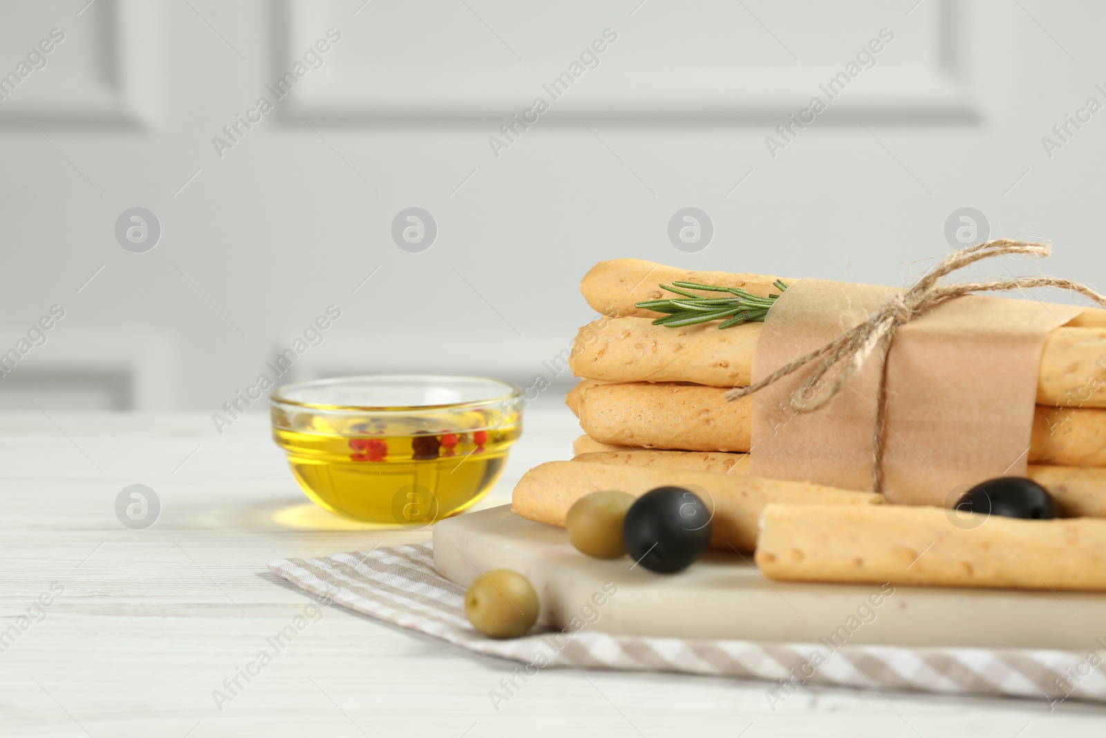 Photo of Tasty grissini with rosemary, olives and oil on white wooden table
