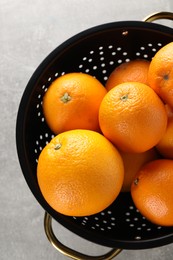 Photo of Fresh ripe oranges in black colander on light grey table, top view