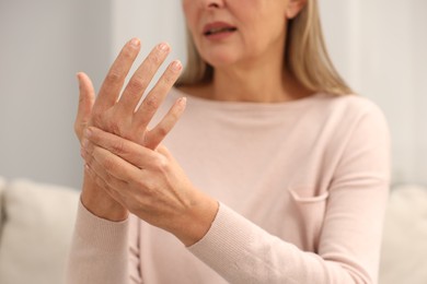 Mature woman suffering from pain in hand indoors, closeup. Rheumatism symptom