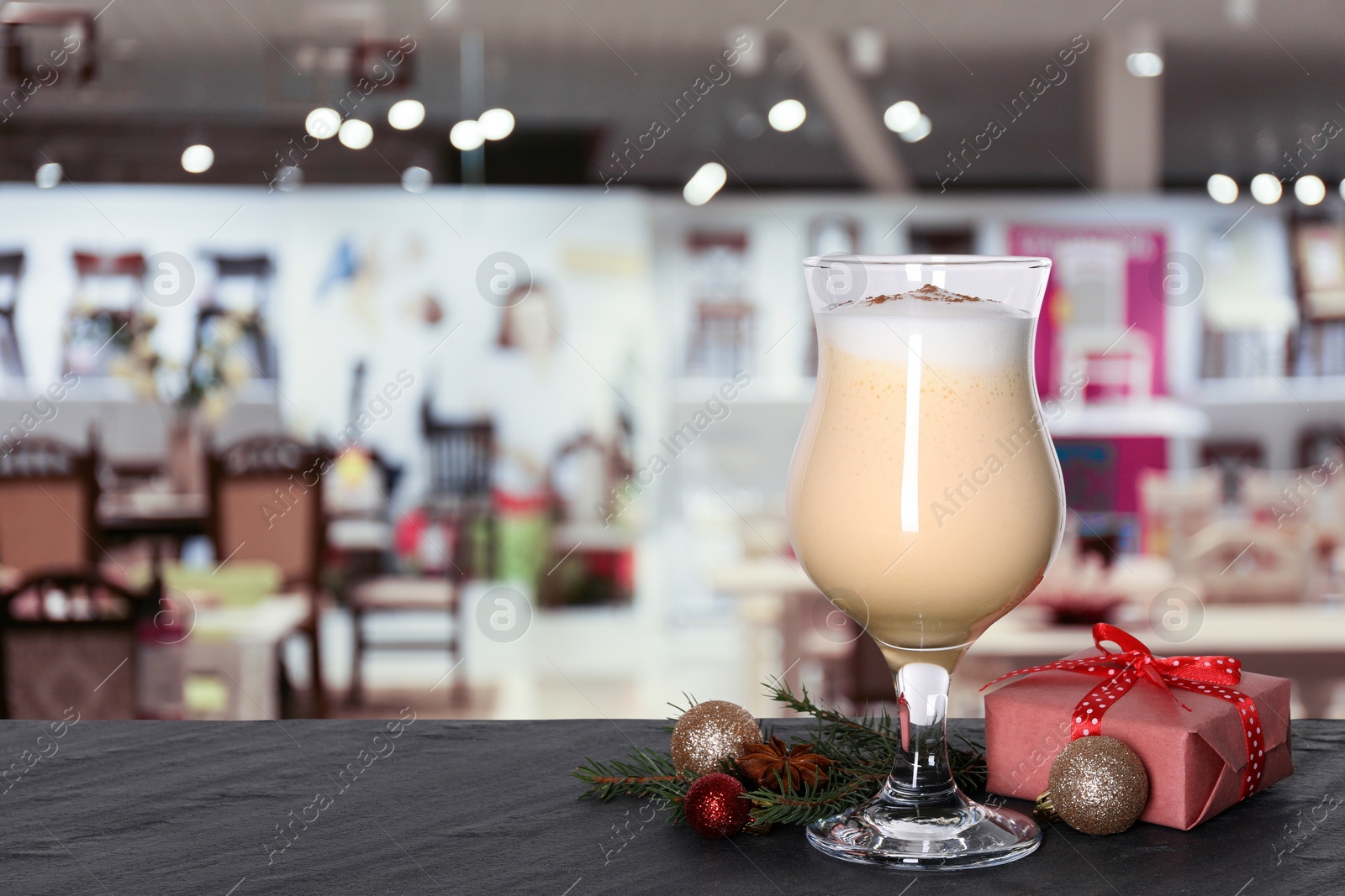 Image of Glass of delicious eggnog, Christmas ornaments, fir tree branches and gift box on dark table in bar, space for text