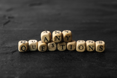 Photo of Wooden cubes with phrase ANY QUESTIONS on black stone table