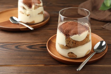 Delicious tiramisu in glasses and spoons on wooden table, closeup