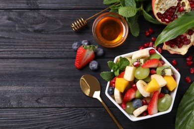 Photo of Delicious fresh fruit salad in bowl on black wooden table, flat lay. Space for text