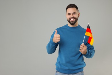 Photo of Young man with flag of Germany showing thumb up on light grey background, space for text