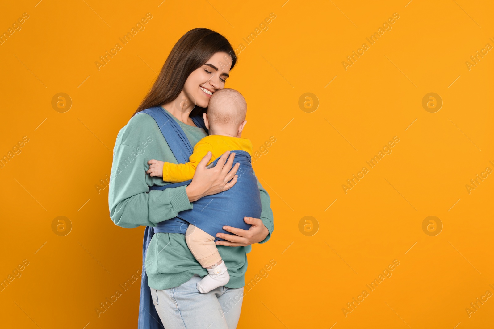 Photo of Mother holding her child in sling (baby carrier) on orange background. Space for text