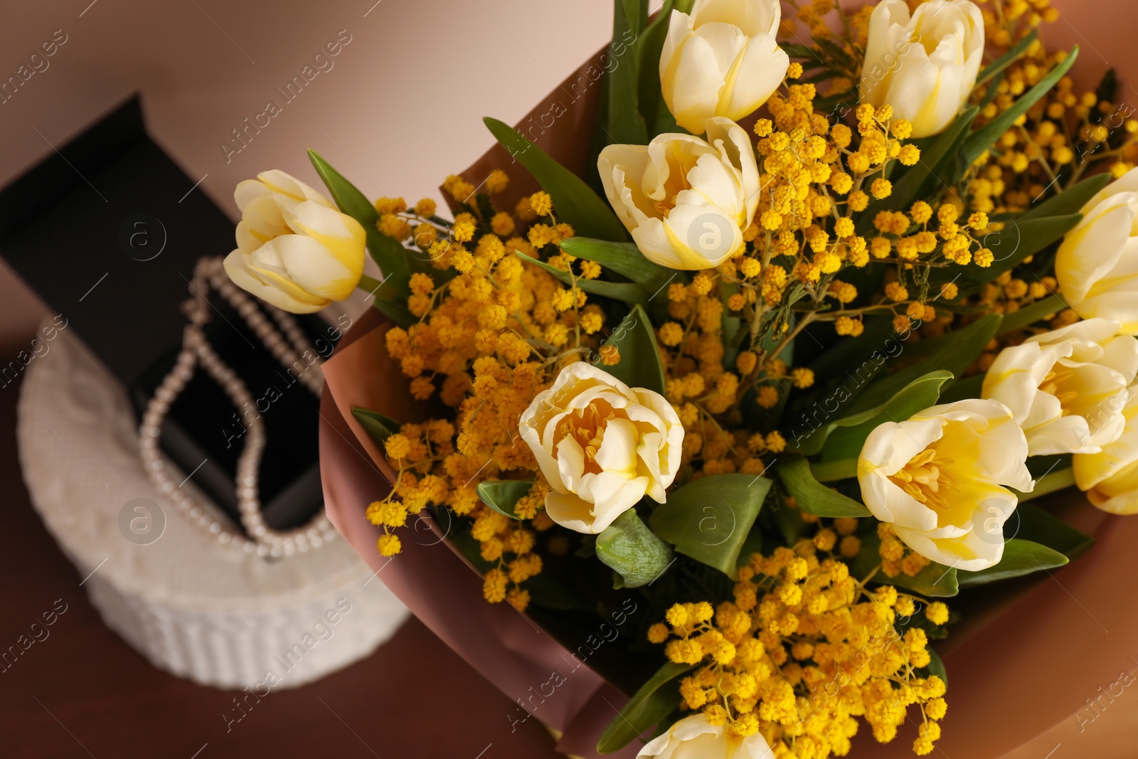 Photo of Bouquet with beautiful spring flowers and necklace on wooden table, above view