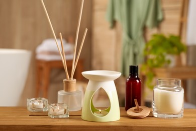 Photo of Aroma lamp, bottle of oil, candles and air reed freshener on wooden table in bathroom