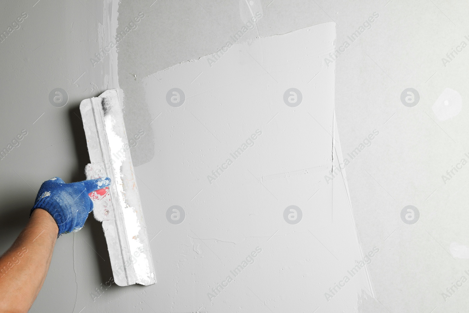 Photo of Professional worker plastering wall with putty knife, closeup