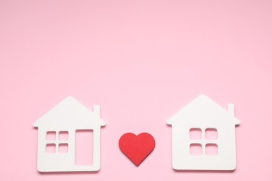 Long-distance relationship concept. Decorative heart between two white house models on pink background, flat lay with space for text