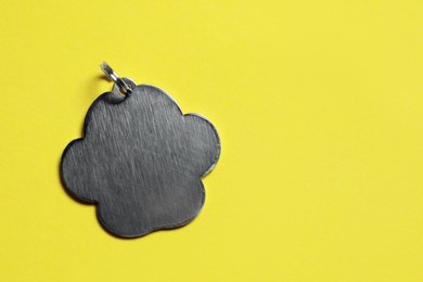 Photo of Silver pet tag with ring on yellow background, top view. Space for text