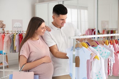 Photo of Happy pregnant woman with her husband choosing baby clothes in store. Shopping concept