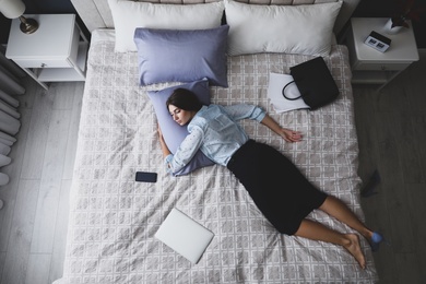 Exhausted businesswoman in office wear sleeping on bed at home after work, above view