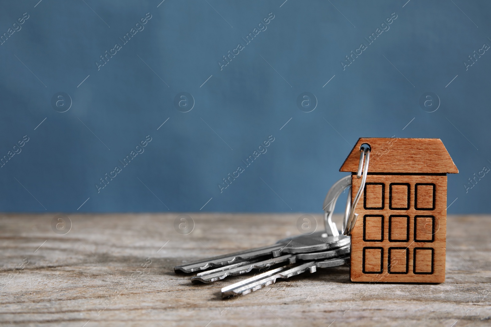 Photo of House keys with trinket on wooden table against color background. Space for text