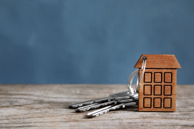 House keys with trinket on wooden table against color background. Space for text