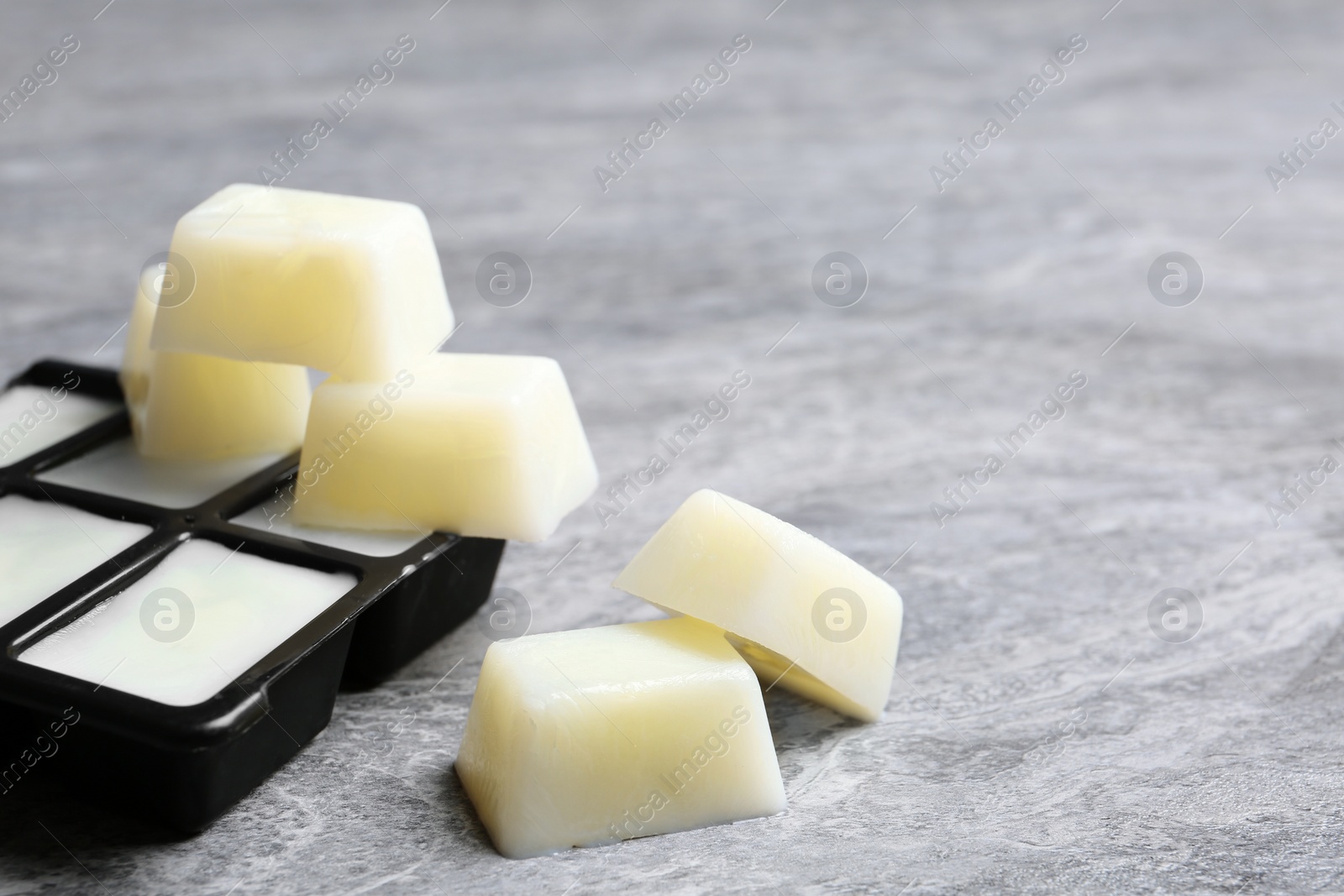 Photo of Ice cubes made with milk and tray on grey table. Space for text