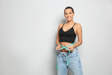 Photo of Slim woman in oversized jeans with measuring tape on light background, space for text. Weight loss