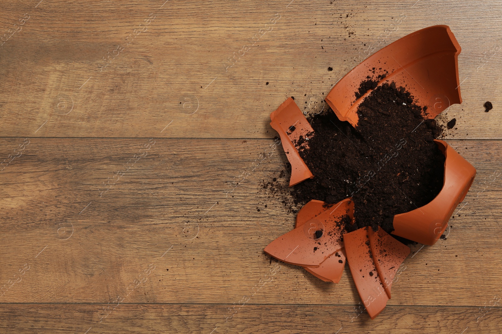Photo of Broken terracotta flower pot with soil on wooden background, flat lay. Space for text