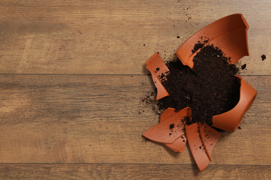 Photo of Broken terracotta flower pot with soil on wooden background, flat lay. Space for text