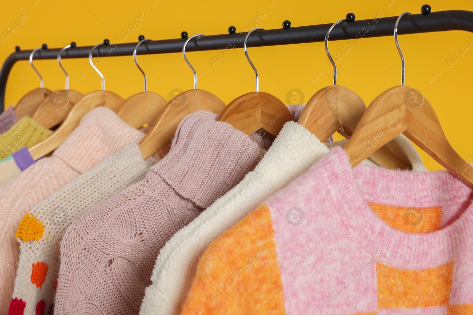 Photo of Rack with stylish women's sweaters on wooden hangers against orange background, closeup
