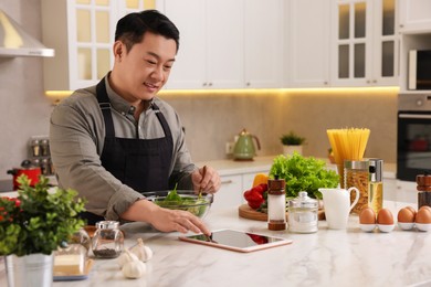 Photo of Man using tablet while cooking in kitchen