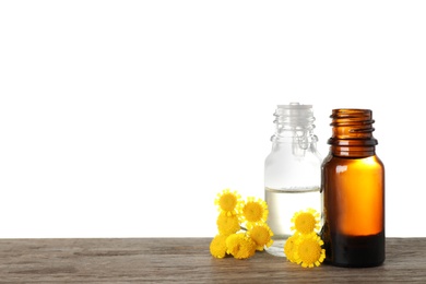 Bottles of essential oil and flowers on wooden table, white background