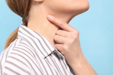 Photo of Woman suffering from sore throat on light blue background, closeup