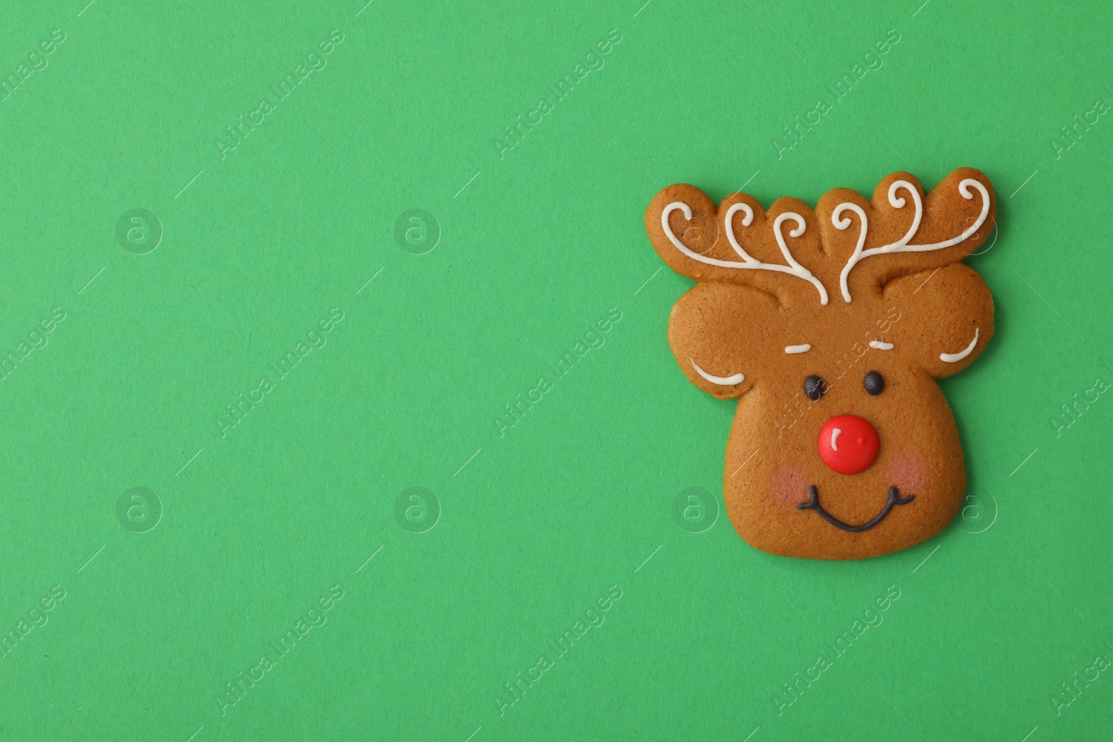 Photo of Christmas deer shaped gingerbread cookie on green background, top view. Space for text